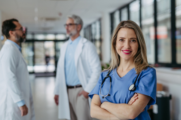 Portrait of female doctor standing in hospital corridor. Beautiful nurse in uniform, stethoscope around neck standing in the modern private clinic, looking at camera.