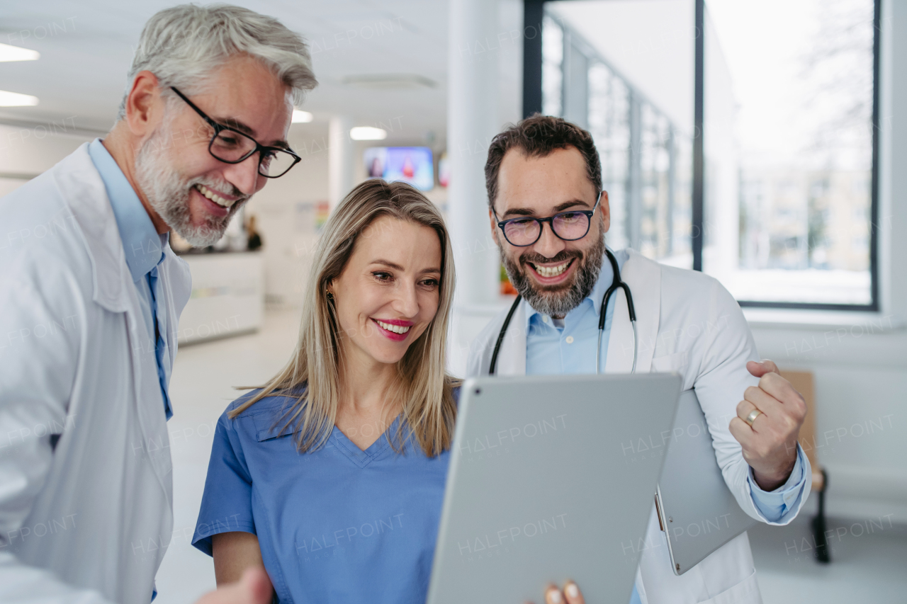 Portrait of doctors and nurse standing in hospital corridor. Healthcare workers in modern private clinic, looking at tablet and smiling.