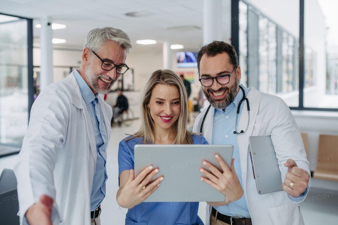 Portrait of doctors and nurse standing in hospital corridor. Healthcare workers in modern private clinic, looking at tablet and smiling.