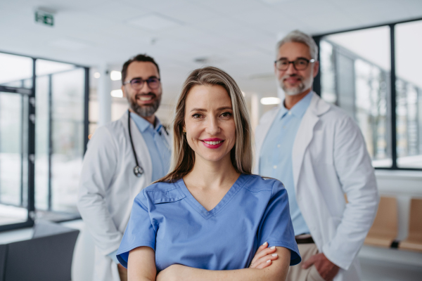 Portrait of female doctor standing in front of male colleagues. Beautiful nurse in uniform, standing in modern private clinic, looking at camera.