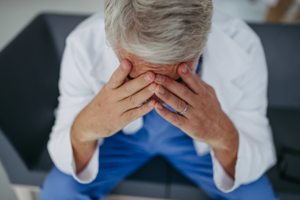 High angle shot of frustrated, exhausted doctor sitting in hospital corridor. Concept of burnout syndrome among doctors, health care workers.