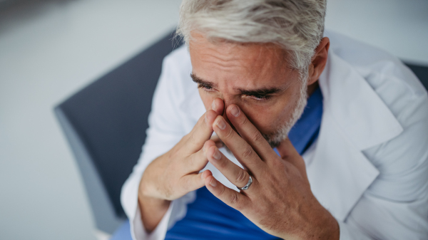 Portrait of frustrated, exhausted doctor sitting in hospital corridor, crying. Concept of burnout syndrome among doctors, health care workers.