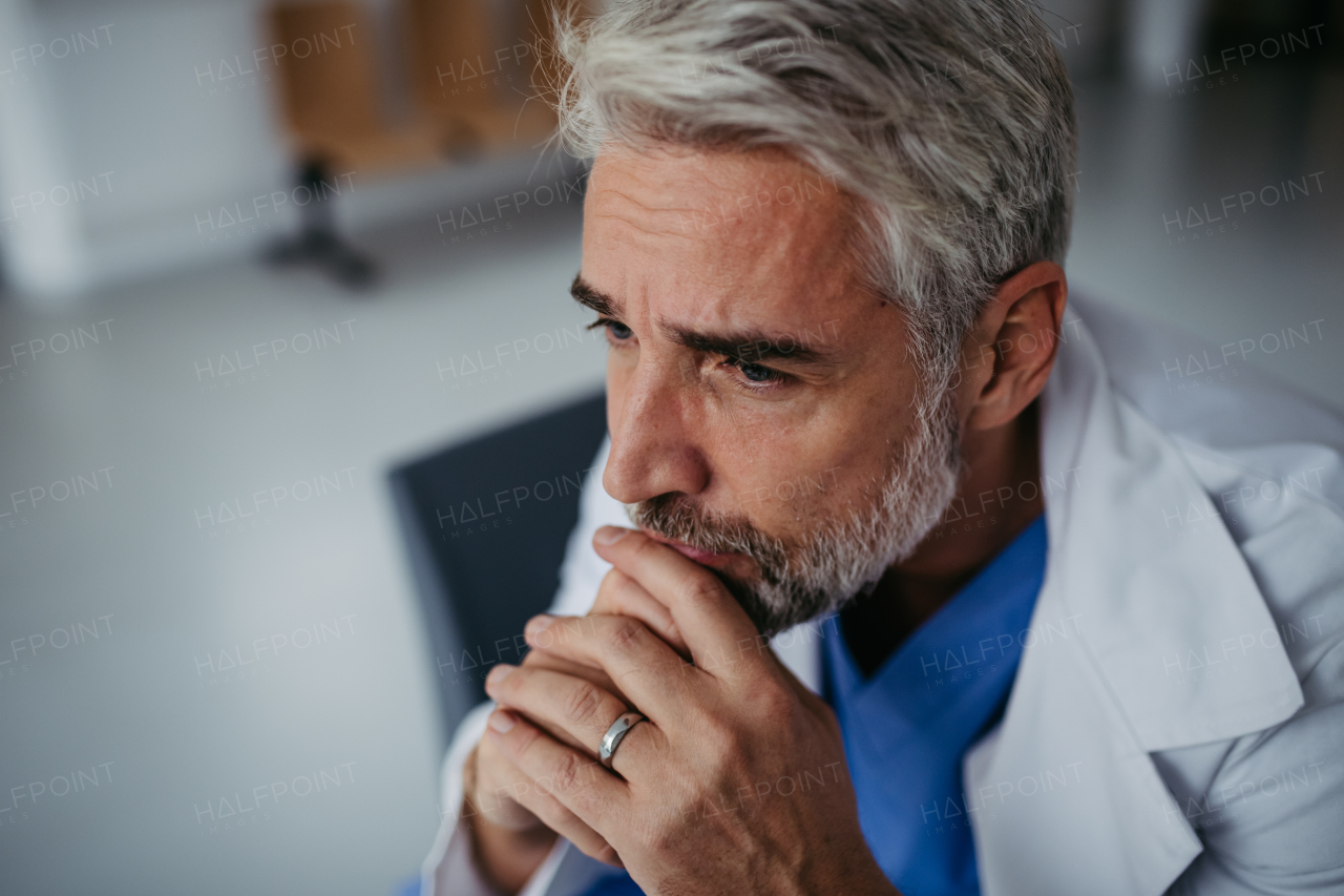 Side view of frustrated, exhausted doctor sitting in hospital corridor. Concept of burnout syndrome among doctors, health care workers.