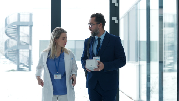 Portrait of pharmaceutical sales representative talking with doctor in medical building. Ambitious male sales representative in suit presenting new medication.