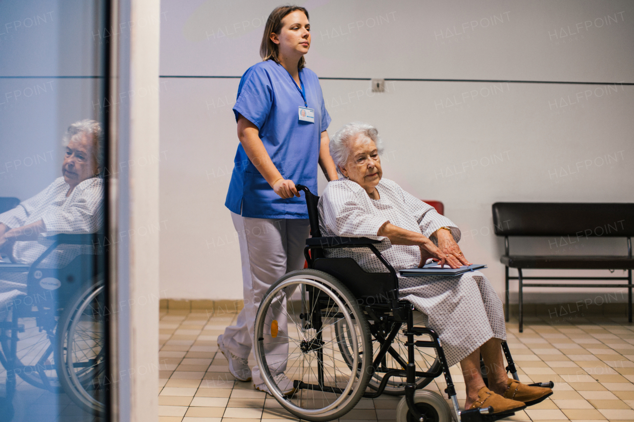 Nurse pushing senior patient in a wheelchair down an outdated hospital corridor. Elderly woman in hospital gown going for surgery.