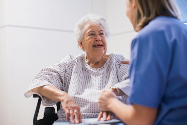 Nurse comforting a scared elderly patient in a wheelchair, holding her hands. Senior woman waiting for examination in the hospital.