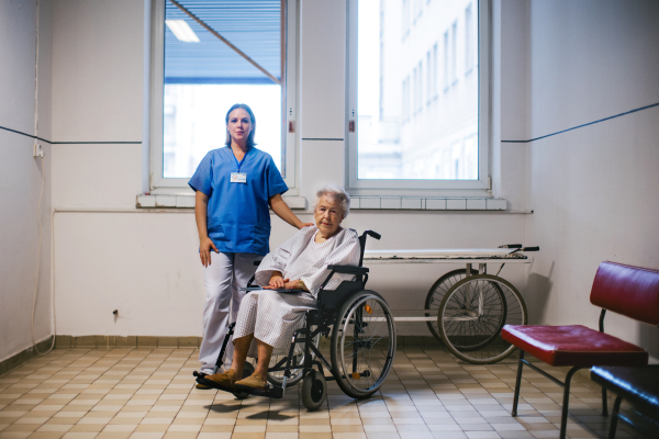 Nurse and senior patient in wheelchair, standing in outdated hospital corridor. Emotional support for older people in hospitals.