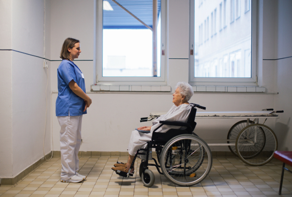 Nurse looking at senior patient in the wheelchair, side view. Emotional support for older people in hospitals.