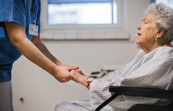 Nurse holding senior patient by hands, comforting scared elderly woman in a wheelchair. Emotional support for older people in hospitals. Close up.