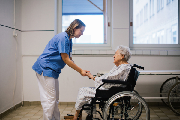 Nurse holding senior patient by hands, consoling scared elderly woman in wheelchair. Emotional support for older people in hospitals. Close up.