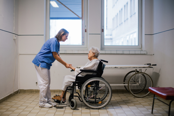 Nurse holding senior patient by hands, consoling scared elderly woman in wheelchair. Emotional support for older people in hospitals. Close up.