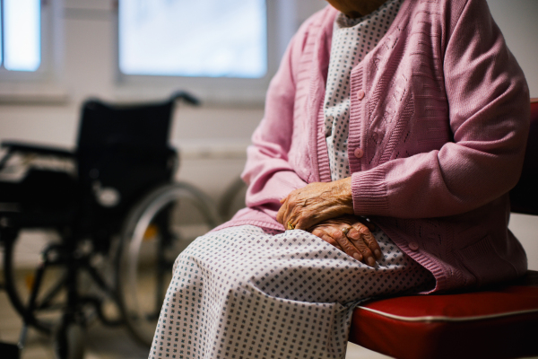 Close up of senior patient waiting for examination in Emergency room, sitting on vinyl chair. Elderly woman in hospital gown waiting for surgery. Outdated hospital with old equpiment and technology.