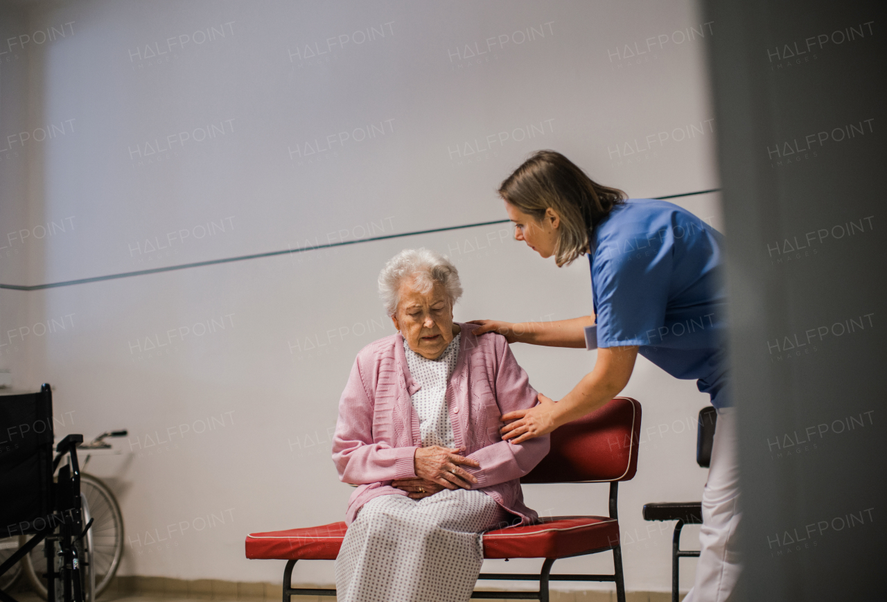 Senior female patient in severe pain, sitting in front of emergency room. Nurse helping elderly woman in hospital gown. Panic attack.