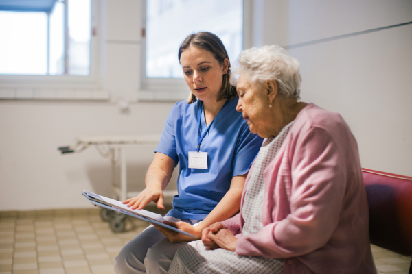 Senior patient talking with nurse, scheduling date and time of next examination. Doctor explaining test resulst, emotional support for elderly woman in hospital.