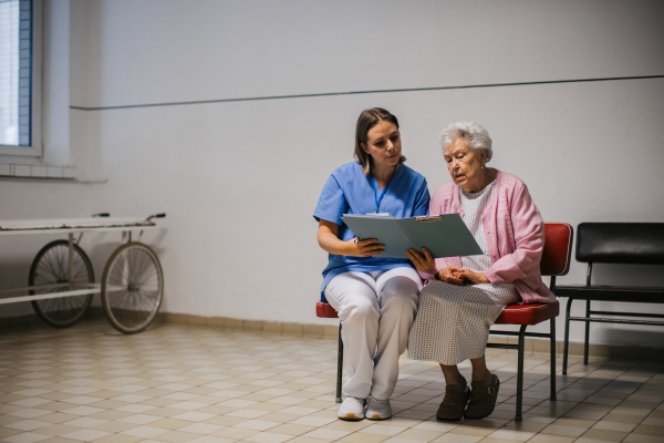 Senior patient talking with nurse, scheduling date and time of next examination. Doctor explaining test resulst, emotional support for elderly woman in hospital.