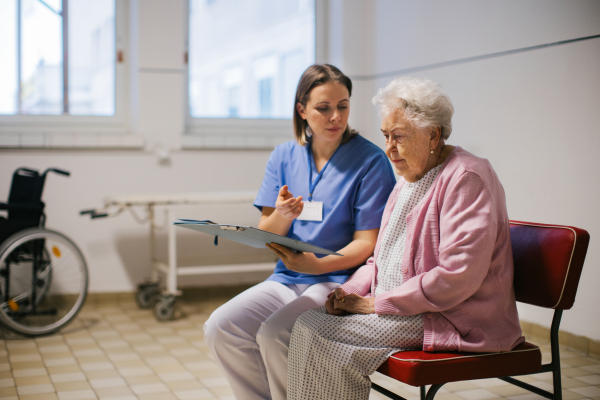 Senior patient talking with nurse, scheduling date and time of next examination. Doctor explaining test resulst, emotional support for elderly woman in hospital.