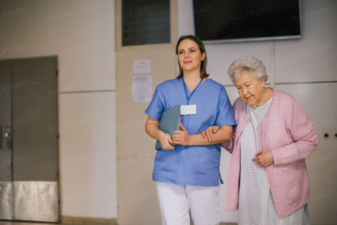 Nurse walking with senior patient, down an outdated hospital corridor. Hospitalized elderly woman in hospital gown is anxious. Emotional support from healthcare workers.