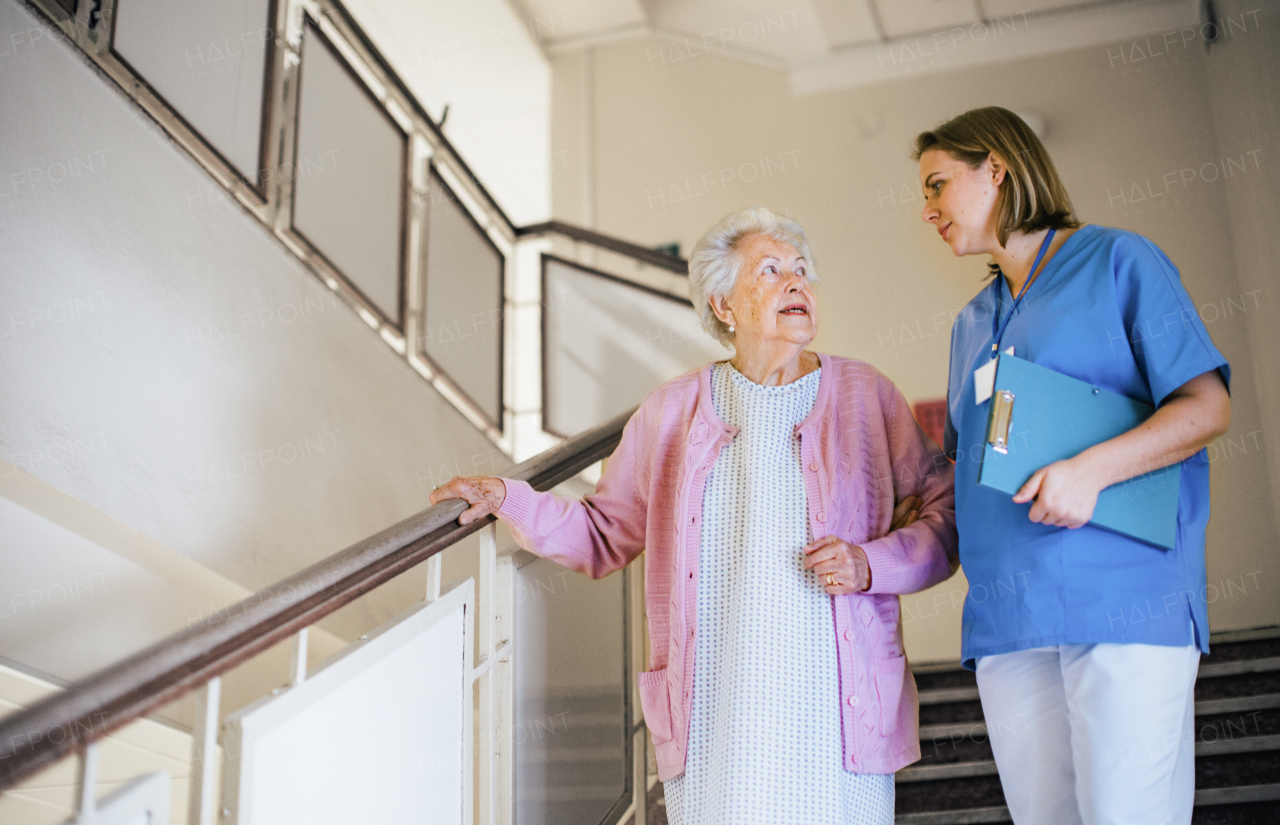 Nurse helping senior patient walk down the stairs. Hospitalized elderly woman in hospital gown is anxious. Emotional support from healthcare workers.