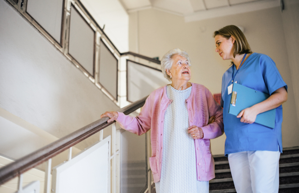 Nurse helping senior patient walk down the stairs. Hospitalized elderly woman in hospital gown is anxious. Emotional support from healthcare workers.