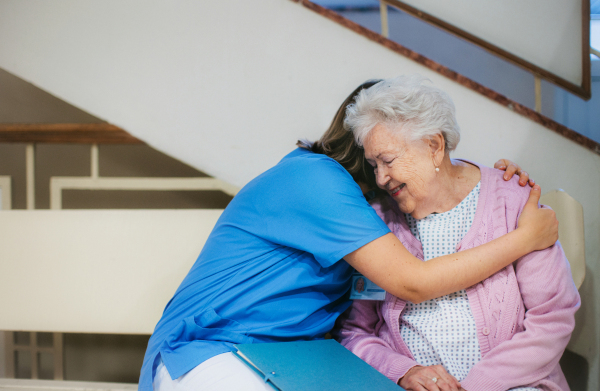 Nurse hugging scared senior patient, sitting on lobby bench, waiting for examination. Elderly patient in hospital gown is anxious. Outdated hospital with old equpiment and technology.