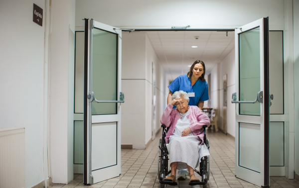 Nurse pushing scared senior patient in a wheelchair down an outdated hospital corridor. Elderly woman in hospital gown going for surgery, feeling anxious.