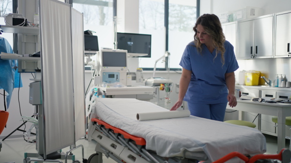 Nurse preparing the examination table in emergency room, examination room. Discarding of used paper and rolling out the fresh sheet of medical exam table paper for next patient.