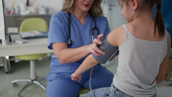 Female Doctor examining young girl, measuring blood pressure, using professional blood pressure monitor. Concept of preventive health care for children.