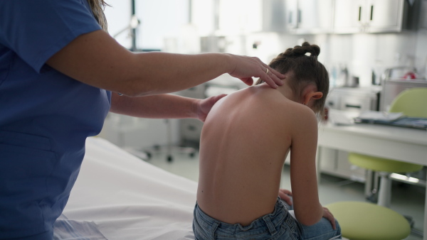 Orthopedist examines the spine, posture, and spinal deformities of little girl. Girl visiting paediatrician for annual preventive physical examination. Concept of preventive health care for children.