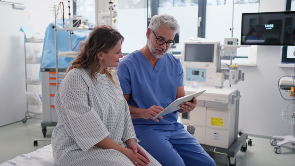 Doctor showing female patient MRI scan on tablet, discussing her test result in emergency room.