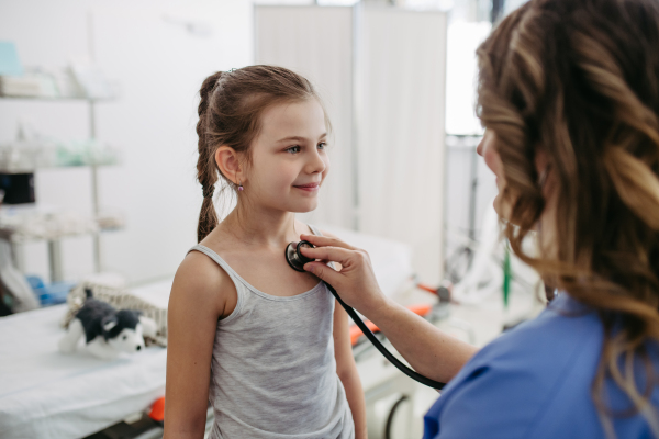 Female Doctor examining young girl, listening to heartbeat, breathing, using stethoscope. Concept of preventive health care for children.