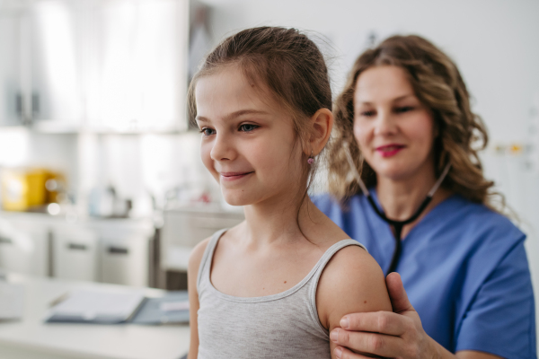 Orthopedist examines the spine, posture, and spinal deformities of little girl. Girl visiting paediatrician for annual preventive physical examination. Concept of preventive health care for children.