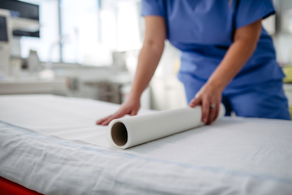 Nurse preparing the examination table in emergency room, examination room. Discarding of used paper and rolling out the fresh sheet of medical exam table paper for next patient.