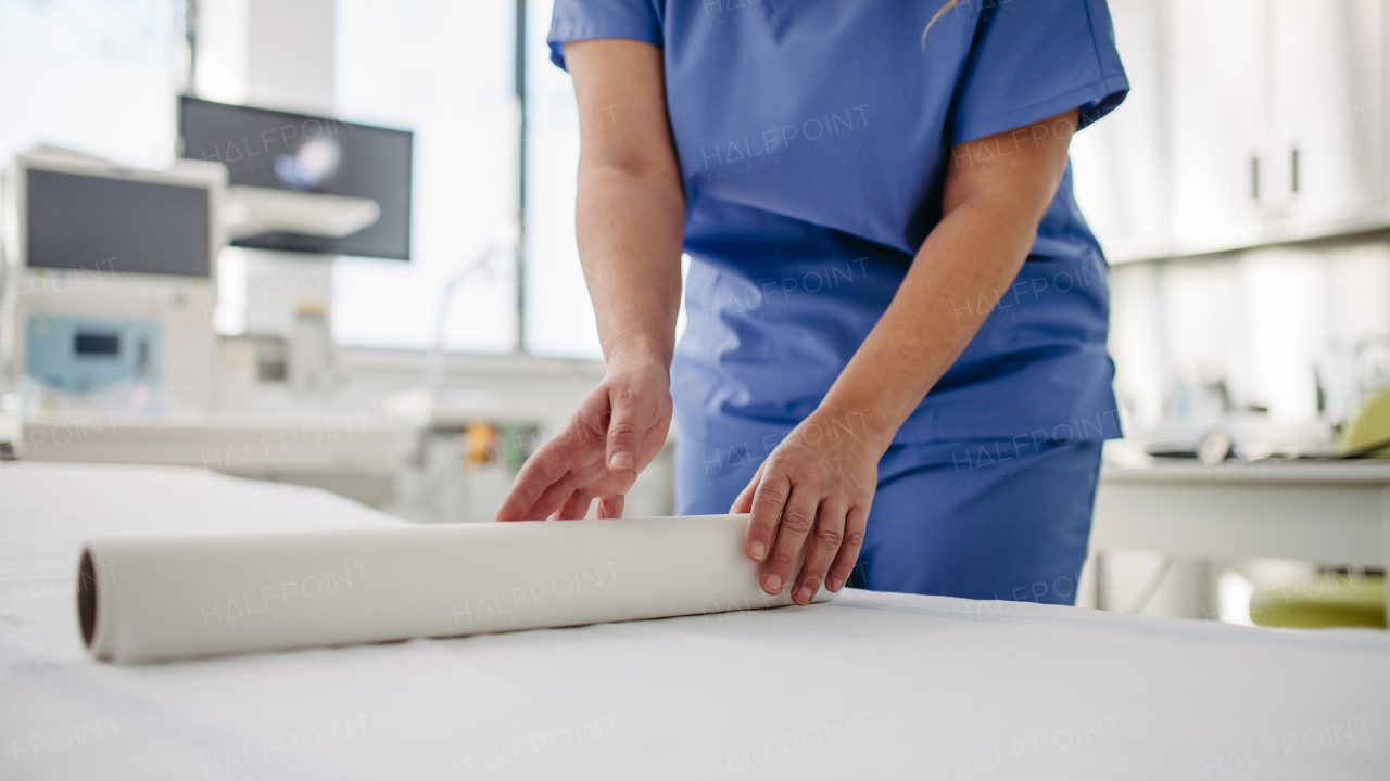 Nurse preparing the examination table in emergency room, examination room. Discarding of used paper and rolling out the fresh sheet of medical exam table paper for next patient.