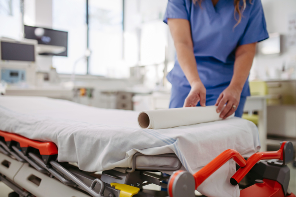 Nurse preparing the examination table in emergency room, examination room. Discarding of used paper and rolling out the fresh sheet of medical exam table paper for next patient.