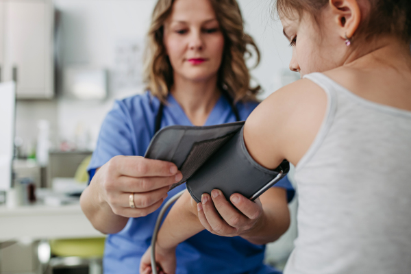 Female Doctor examining young girl, measuring blood pressure, using professional blood pressure monitor. Concept of preventive health care for children.