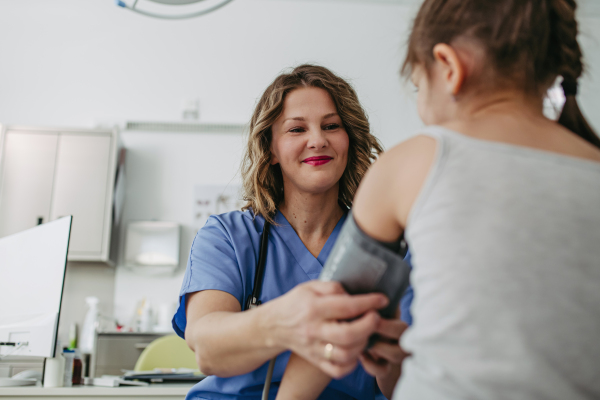 Female Doctor examining young girl, measuring blood pressure, using professional blood pressure monitor. Concept of preventive health care for children.