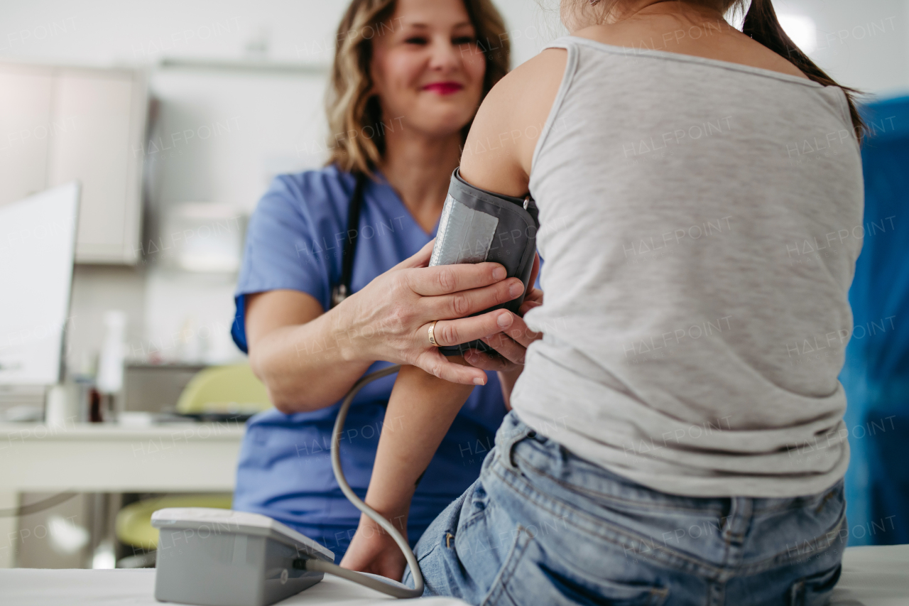 Female Doctor examining young girl, measuring blood pressure, using professional blood pressure monitor. Concept of preventive health care for children.