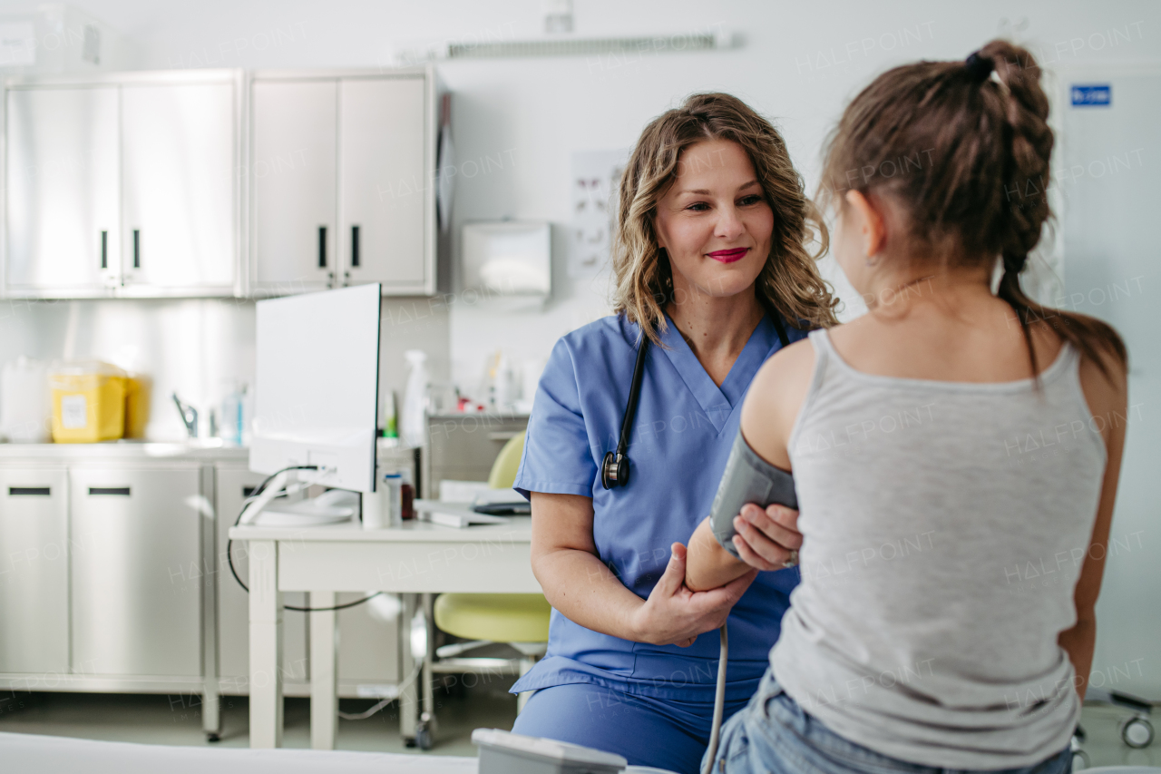 Female Doctor examining young girl, measuring blood pressure, using professional blood pressure monitor. Concept of preventive health care for children.