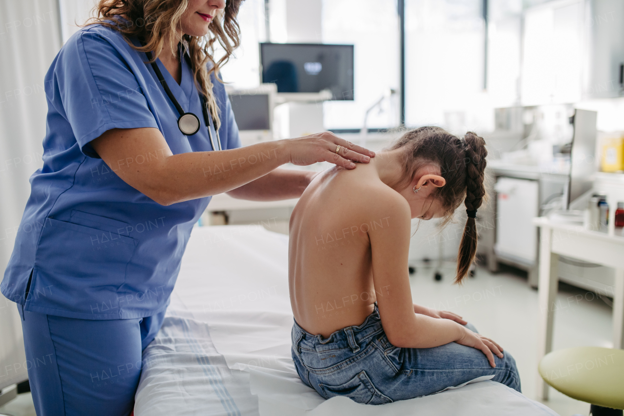 Orthopedist examines the spine, posture, and spinal deformities of little girl. Girl visiting paediatrician for annual preventive physical examination. Concept of preventive health care for children.