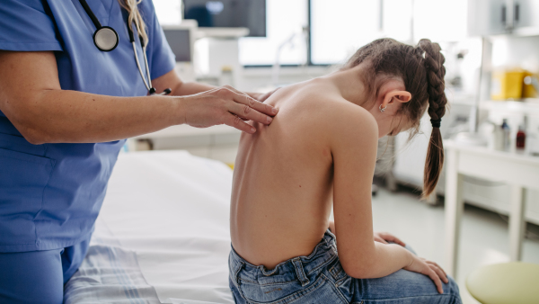 Orthopedist examines the spine, posture, and spinal deformities of little girl. Girl visiting paediatrician for annual preventive physical examination. Concept of preventive health care for children.