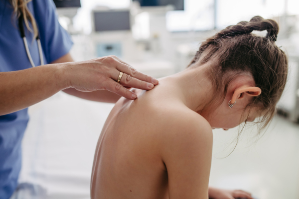 Orthopedist examines the spine, posture, and spinal deformities of little girl. Girl visiting paediatrician for annual preventive physical examination. Concept of preventive health care for children.