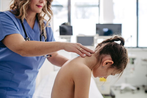 Orthopedist examines the spine, posture, and spinal deformities of little girl. Girl visiting paediatrician for annual preventive physical examination. Concept of preventive health care for children.