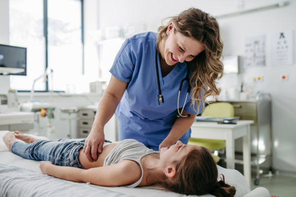 Female doctor palpating girl's abdomen, using hands and steady pressure. Concept of preventive health care for children.