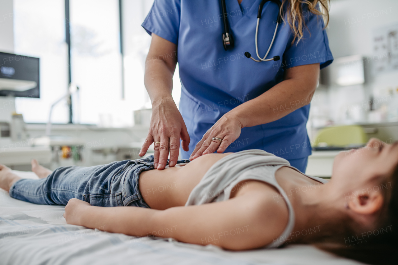 Female doctor palpating girl's abdomen, using hands and steady pressure. Concept of preventive health care for children.