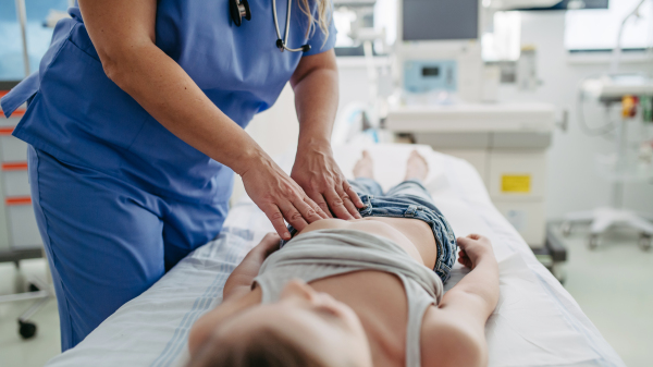 Close up of doctor palpating girl's abdomen, using hands and steady pressure on belly. Concept of preventive health care for children.