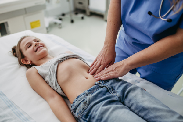 Close up of doctor palpating girl's abdomen, using hands and steady pressure on belly. Concept of preventive health care for children.