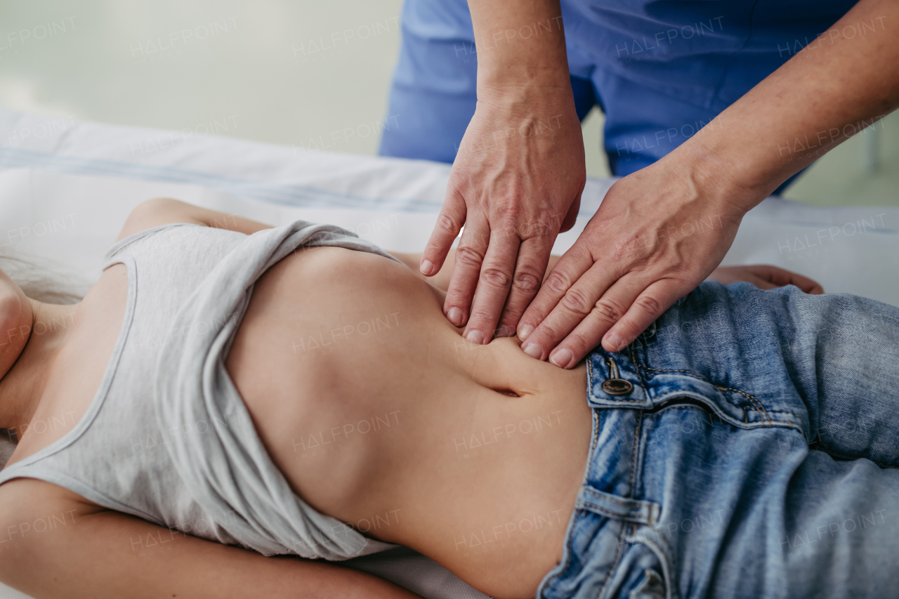 Close up of doctor palpating girl's abdomen, using hands and steady pressure on belly. Concept of preventive health care for children.