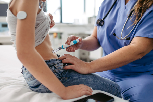 Nurse injecting insulin in diabetic young girl belly. Close up of young girl with type 1 diabetes taking insuling with syringe needle.