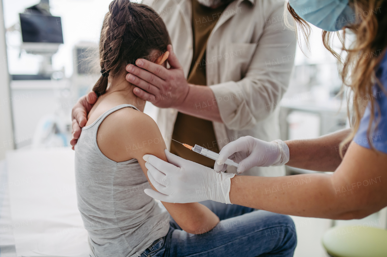 Routine vaccinations for a child. Father holding small girl while pediatrician injecting vaccine into her arm.