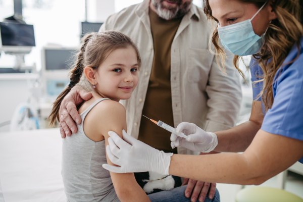 Routine vaccinations for a child. Father holding small girl while pediatrician injecting vaccine into her arm.